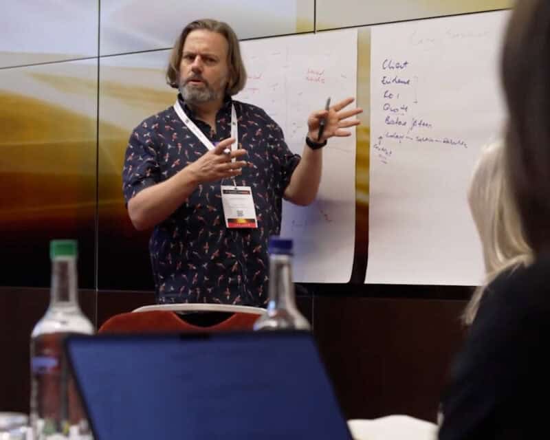 Thumbnail for the consultancy video, with a play button. David stands alongside some chart paper, tacked to a wall. His handwriting is terrible. He’s wearing a lanyard, and is speaking with his hands, which looks like a weird dance. He’s wearing a blue shirt with parrots on it.